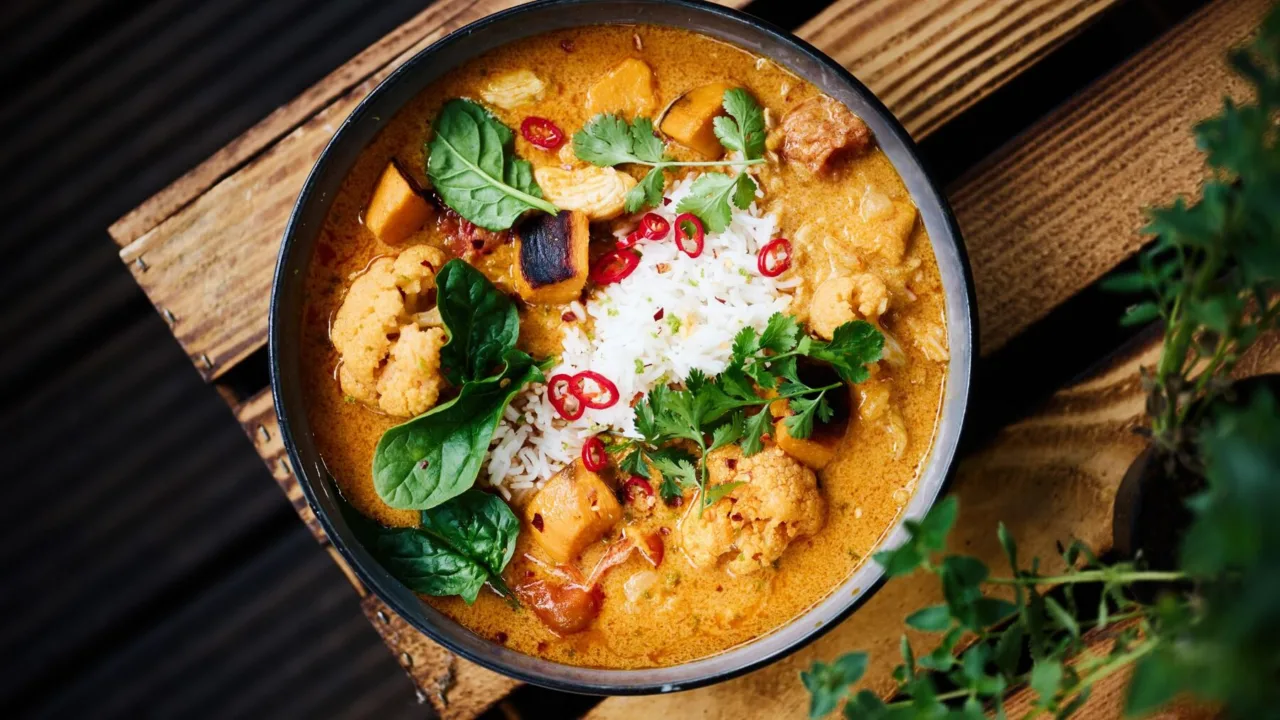 Krémes zöldséges curry rizzsel, chilivel és friss bazsalikommal egy sötét tálban.